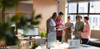 Stop Paying for Leads: 75 Free Directories That Convert Five business professionals collaborate around computer workstations in a modern open-plan office, illustrating the entrepreneurial environment where free directory listings support business growth.