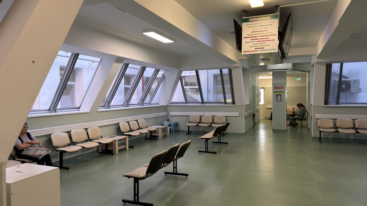 A modern medical waiting room with bench seating and digital display screen, illustrating contemporary outpatient clinic environments designed for improved patient experience.
