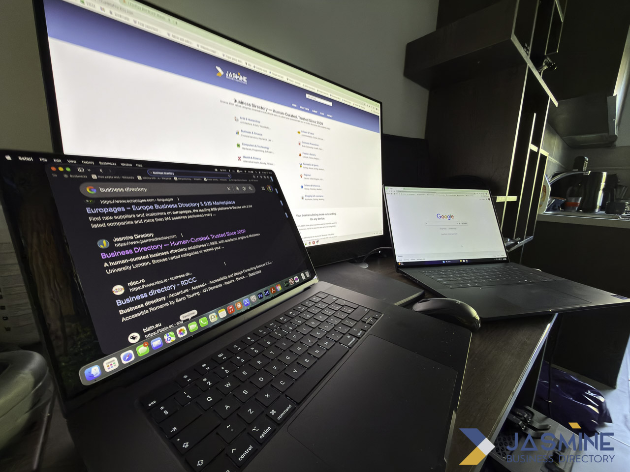 Dark workspace with laptop, external monitor, and smartphone displaying business directory listings and Google search homepage, illustrating comparison of customer discovery channels.