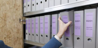 Hand reaching for labeled binders on metal office shelving, demonstrating the systematic organization principles central to effective database schema design and data retrieval.