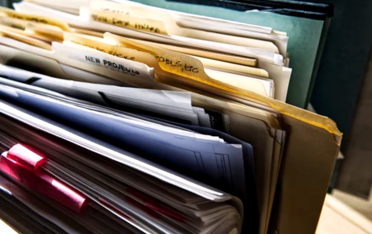 Organized file folders and notebooks in a teal storage box with visible project labels, illustrating systematic documentation approaches relevant to directory submission workflows.