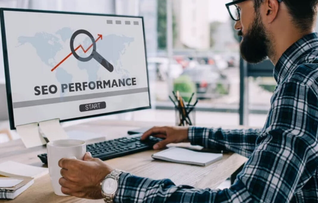 Professional analyzing SEO performance metrics illustrates how technical optimization drives business revenue Office worker in plaid shirt views computer monitor showing SEO performance dashboard with upward trend arrow, representing the connection between website optimization and revenue generation.