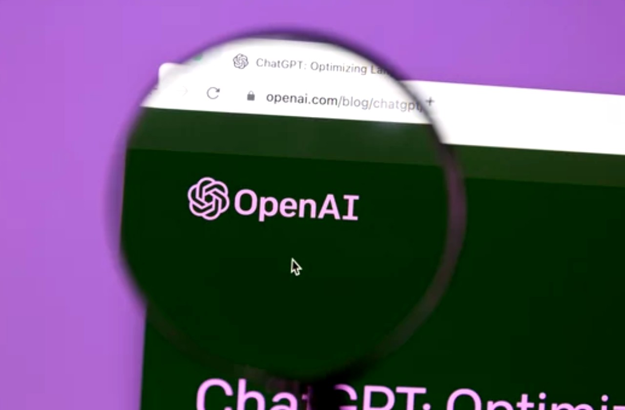 Magnifying glass focusing on OpenAI website displaying ChatGPT on computer screen, illustrating technology for marketing strategy innovation and automation.