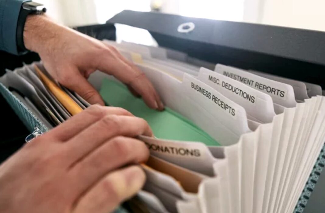 Systematic financial organization illustrates structured approach to managing multiple directory revenue streams Hands organizing labeled financial documents in an accordion folder on a desk, representing the systematic categorization required for multi-faceted directory monetization models.