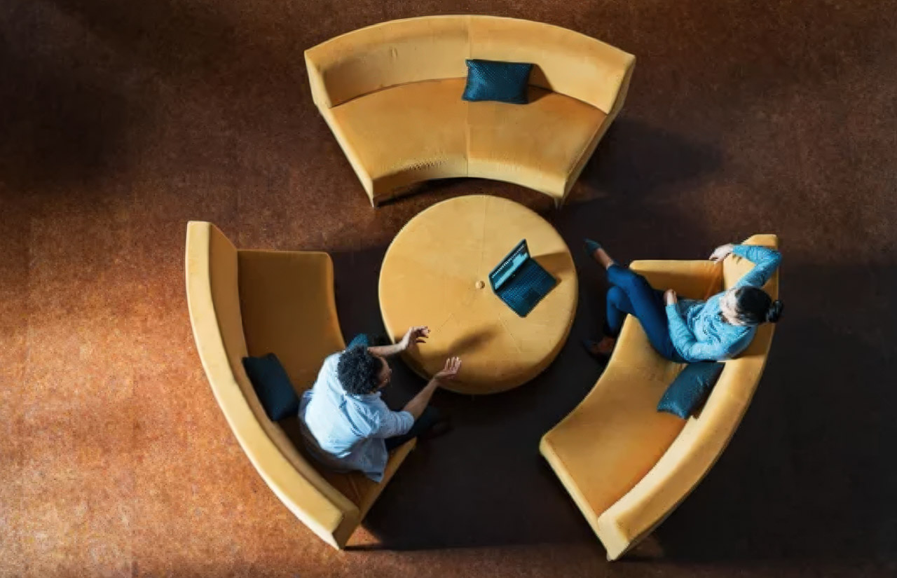 Overhead view of two people meeting at a round table with modular yellow seating, illustrating collaborative workspace approaches central to modern directory partnerships.