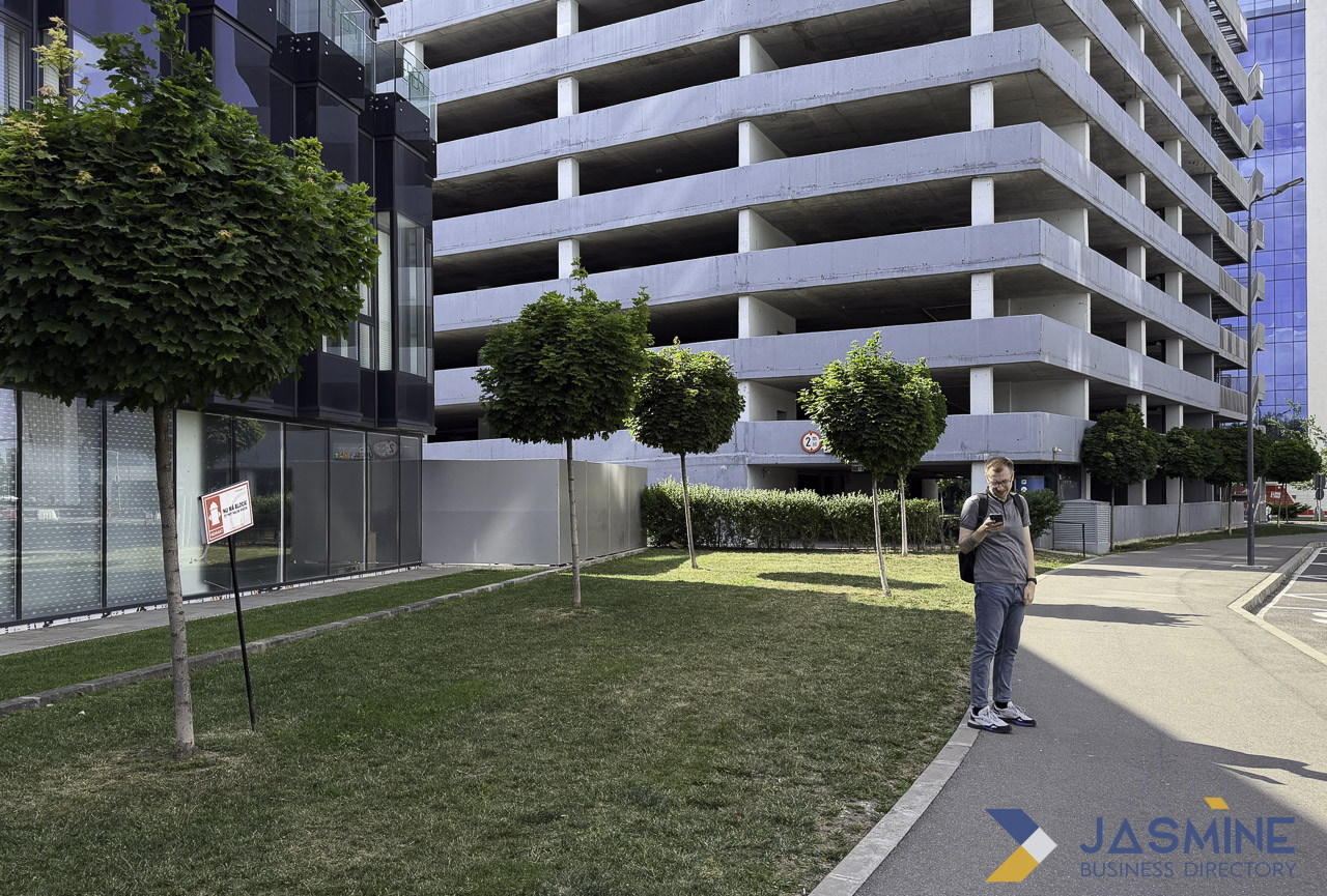 Pedestrian with smartphone walking past modern residential buildings and parking structure, illustrating mobile local search behavior in urban neighborhoods.