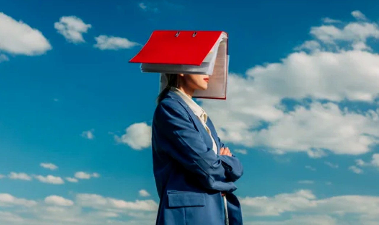 Person in blue suit wearing a red-roofed binder structure on their head against a cloudy sky, representing the organizational burden businesses face with online visibility.