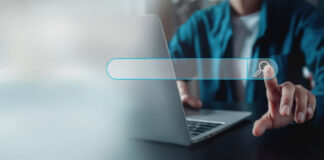 What is the modern Yellow Pages? Person in teal clothing points to a floating digital search bar above a laptop, illustrating the modern interface of business directory services.