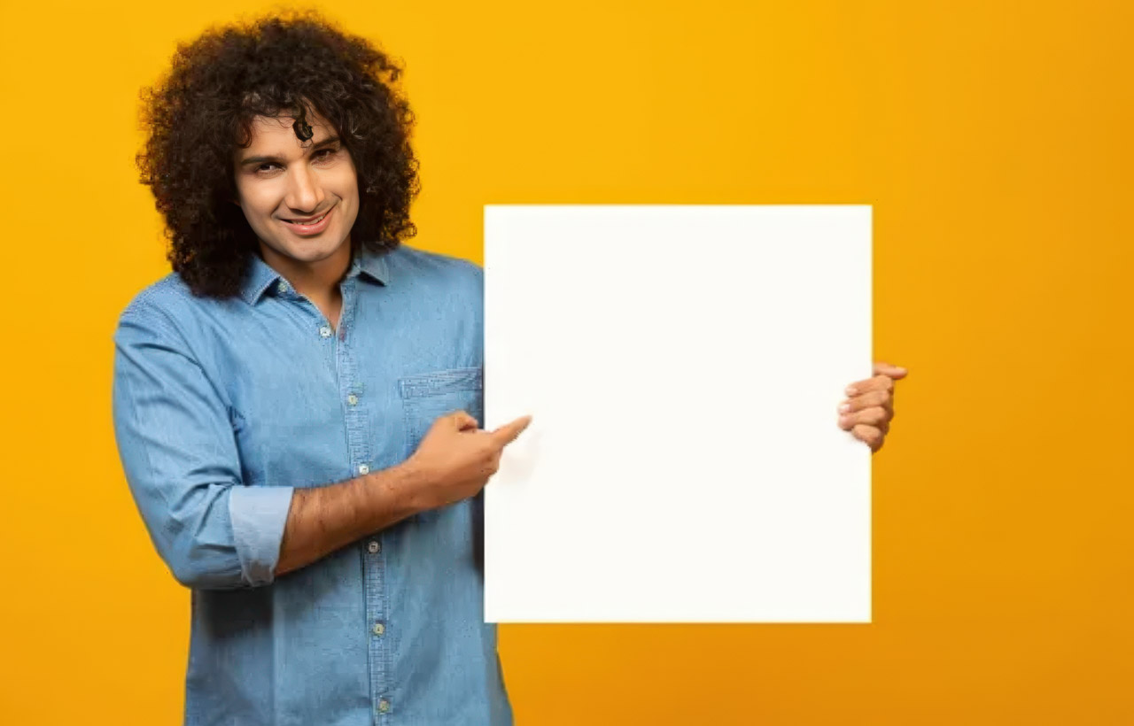Person with curly hair holds white blank sign against yellow background in studio portrait, representing advertising message presentation and communication concepts.