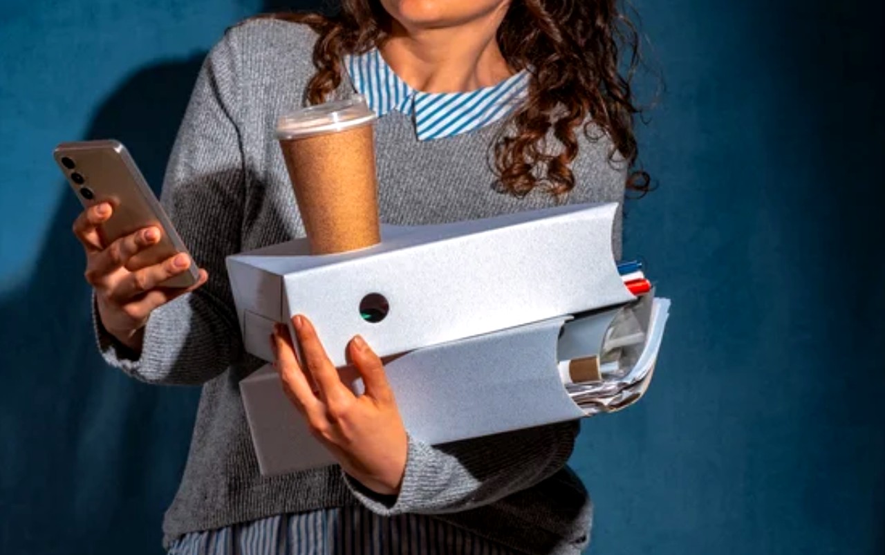 Person holding smartphone and takeout coffee against blue wall, representing mobile-first business owners managing their online presence and AI search visibility.