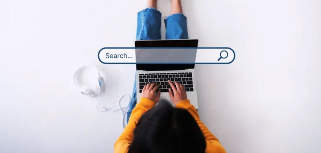 Online search and discovery concept illustrating business visibility challenges Overhead view of person typing on laptop with search bar overlay graphic, representing the process of searching for businesses online and directory optimization.