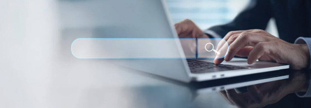 Hands typing on laptop illustrate user search behavior and query formulation psychology Close-up of hands typing on laptop keyboard with translucent search bar overlay, illustrating user behavior when formulating search queries.