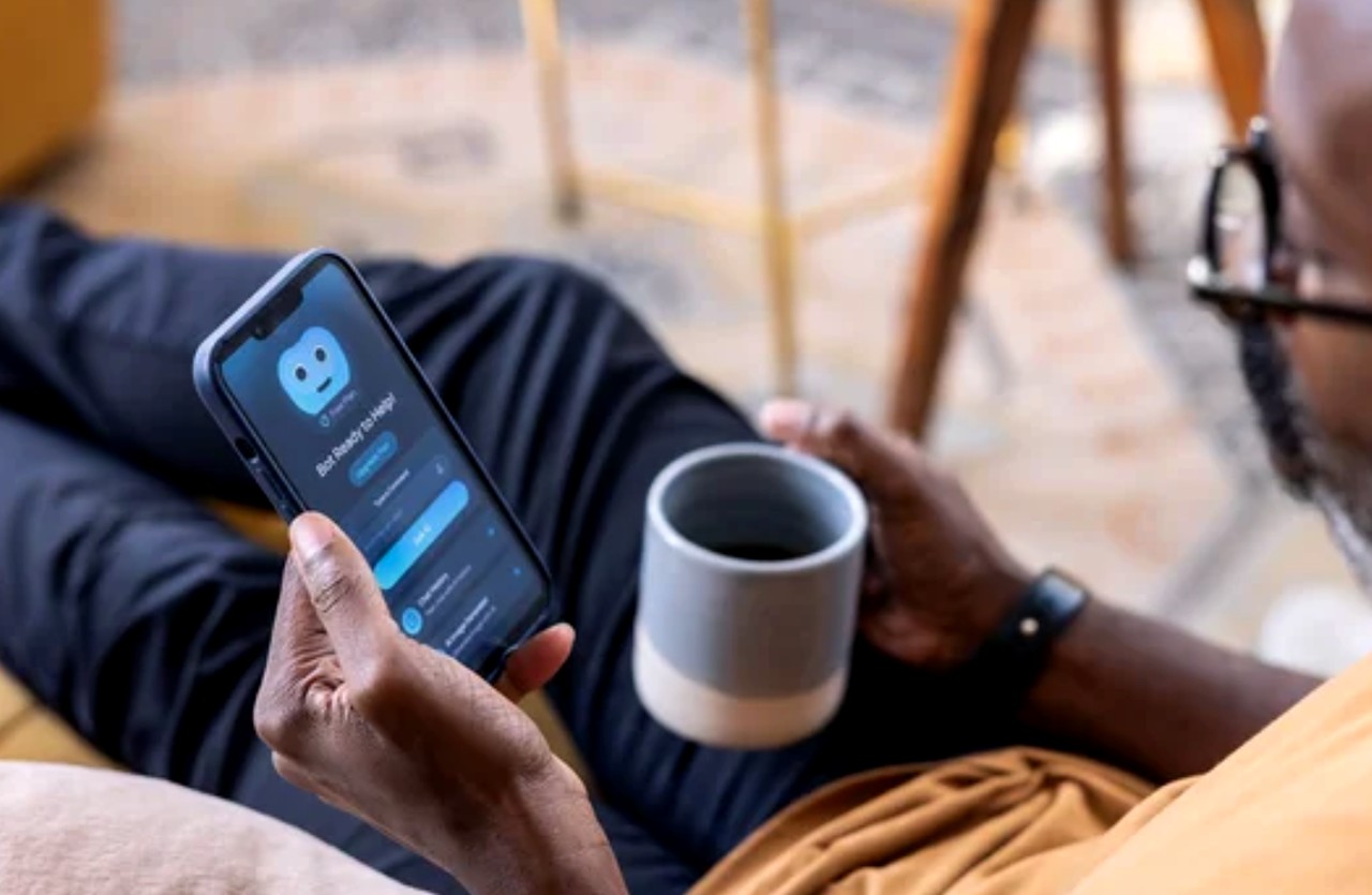 Person in navy sweater using smartphone with visible app interface while holding ceramic coffee mug, illustrating modern customer service interactions through mobile technology.