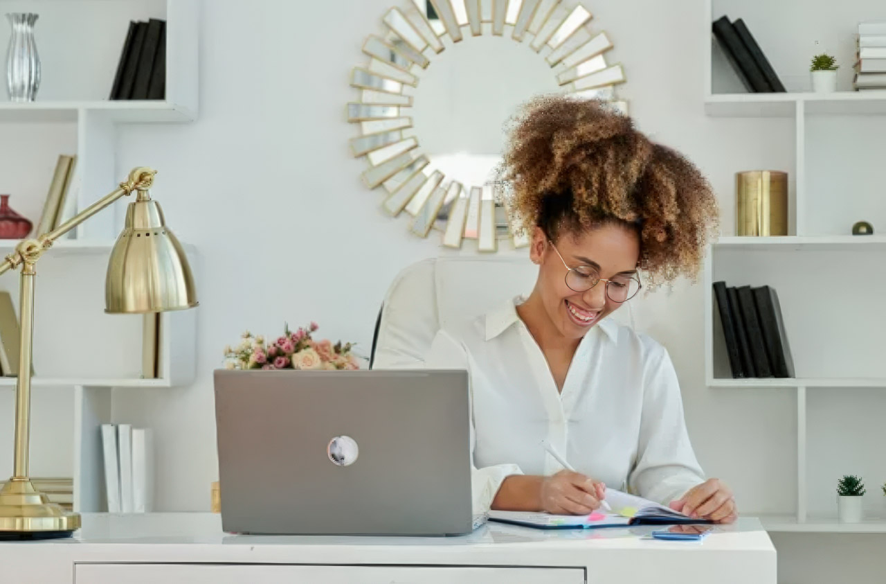 Person seated at organized white desk with laptop and notebook in bright home office, representing a modern content creator's workspace for blogging and digital writing.