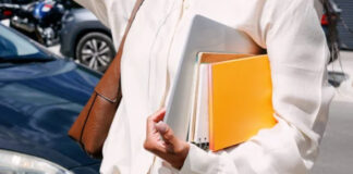 Small Business Owners: Stop Guessing, Use Directories Person in cream blouse carrying books and laptop with leather bag on street, representing a small business owner prepared for professional research.