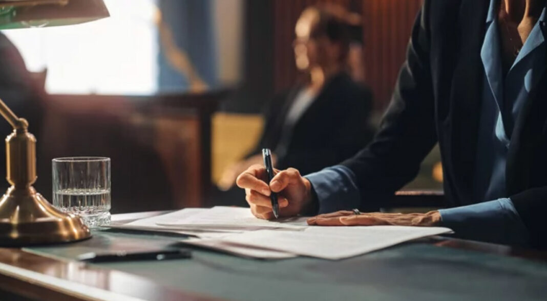 Professional editing documents at desk, illustrating human oversight in content refinement process Person in business attire writing on documents at a desk with brass lamp and water glass, representing the human editing process essential for refining AI-generated content.
