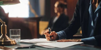 How to properly edit AI-generated content? Person in business attire writing on documents at a desk with brass lamp and water glass, representing the human editing process essential for refining AI-generated content.