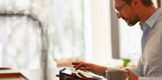 Professional man wearing glasses reviews content on a tablet at his wooden desk, representing the process of updating and managing digital content.