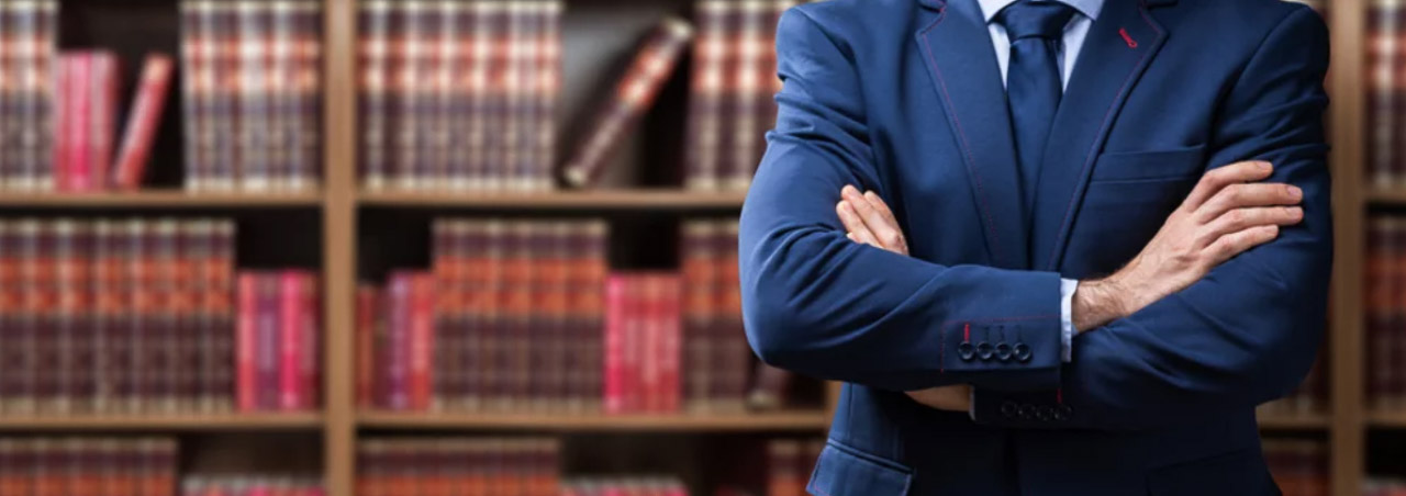 Professional in navy suit stands with crossed arms before a law library bookcase, representing the shift toward credentialed expert authority in business.