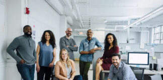Privacy-Preserving Ad Tech: Understanding Data Clean Rooms Seven professionals pose together in a modern open-plan office with workstations and monitors, representing collaborative teams working on privacy-preserving advertising technology.
