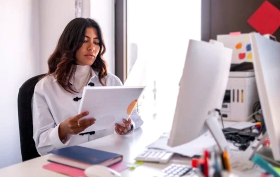 Professional reviewing work at organized desk workspace illustrates approach to improving image quality and workflow Professional woman reviewing documents at organized office desk with computer monitor and supplies, illustrating focused workflow for improving image quality and editing processes.