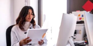 How can I make my images better? Professional woman reviewing documents at organized office desk with computer monitor and supplies, illustrating focused workflow for improving image quality and editing processes.
