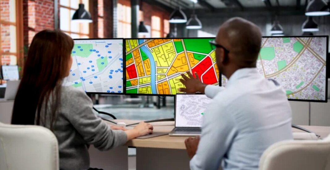 Geographic data analysis illustrates the scope difference between local and global directory strategies Two professionals examine multiple computer monitors displaying various geographic maps and zoning data, illustrating the analytical approach to local versus global business directory strategy.