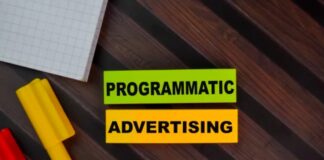 Native Advertising in the Age of AI Summaries Flat lay photograph of a programmatic advertising text banner on a wood surface with colored blocks and graph paper, representing automated advertising strategies in digital marketing.