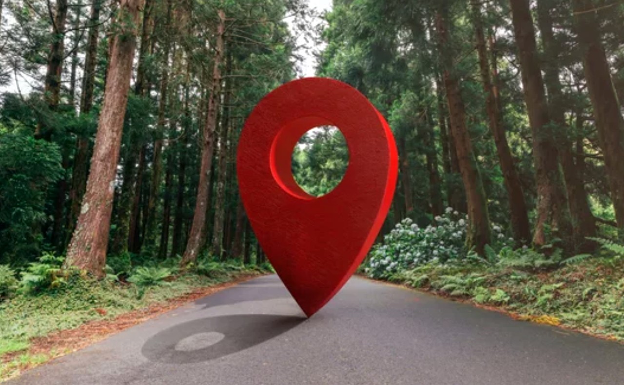 A red digital location pin marker overlaid on a forested road, representing geofencing and location-based technology used in retail proximity marketing.