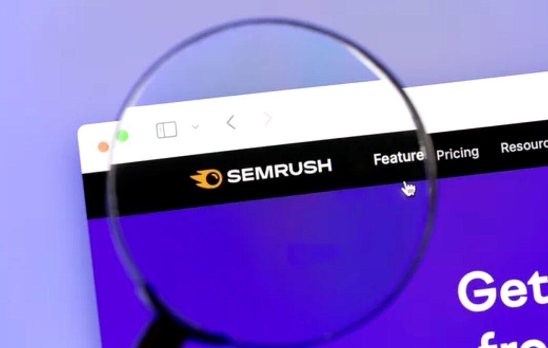 Magnified view of analytics platform symbolizes the careful examination needed to monitor website errors Magnifying glass held up to computer screen displaying SEMRUSH analytics website, representing the detailed attention required for website error monitoring and maintenance.