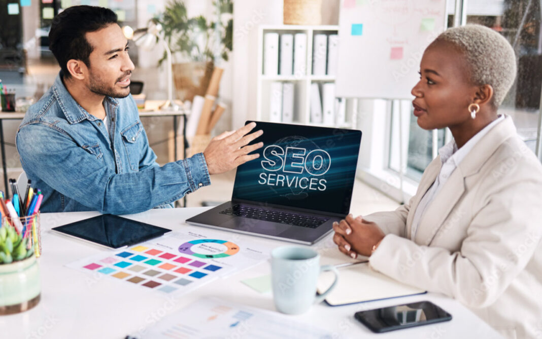 Digital marketing professionals collaborate on SEO strategy to improve directory listings and search rankings Two business professionals meet at a desk with a laptop displaying SEO services, discussing strategies for strengthening directory listings and search engine rankings.