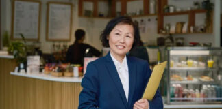 The One Thing Every Local Business Needs Professional woman in business suit holding folder stands in café interior, representing local business ownership and entrepreneurial presence in neighborhood commerce.