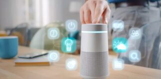 Sound and Voice Branding: Marketing to Smart Speakers and Hearables Hand interacting with cylindrical smart speaker displaying holographic control icons on wooden table, illustrating voice-first technology for audio branding applications.