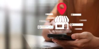 Person holds smartphone displaying digital overlay graphics of storefront icon, location marker, and star ratings above laptop, illustrating how customers discover businesses through mobile search results.
