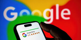 The Role of Trust Scores in Ad Bidding Algorithms Hand holding smartphone displaying Google's 5-star rating interface with blurred monitor in background, representing trust score systems used in digital advertising platforms.