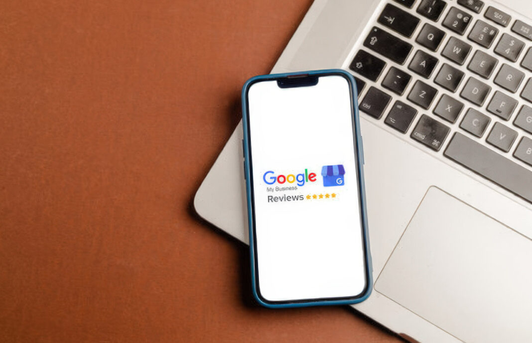 Google Reviews interface on smartphone illustrates digital directory customer feedback systems in Australia Smartphone displaying Google My Business Reviews interface with five-star rating rests on laptop keyboard, representing customer review systems adopted by Australian directories.