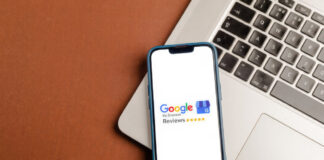 Smartphone displaying Google My Business Reviews interface with five-star rating rests on laptop keyboard, representing customer review systems adopted by Australian directories.