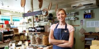 The best QMS software for companies in the food, chemicals and consumer goods sectors Woman in striped apron behind wooden cheese counter in specialty food shop, illustrating focused niche marketing and personalized customer service in independent retail.
