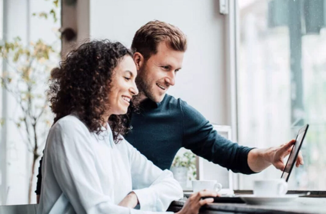 Business professionals collaborate on digital strategy illustrating cross-platform identity management Two professionals stand together reviewing content on a tablet in a bright modern office, representing collaborative business profile management across digital platforms.