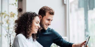 Local Business Schema: The “SameAs” Property Importance Two professionals stand together reviewing content on a tablet in a bright modern office, representing collaborative business profile management across digital platforms.