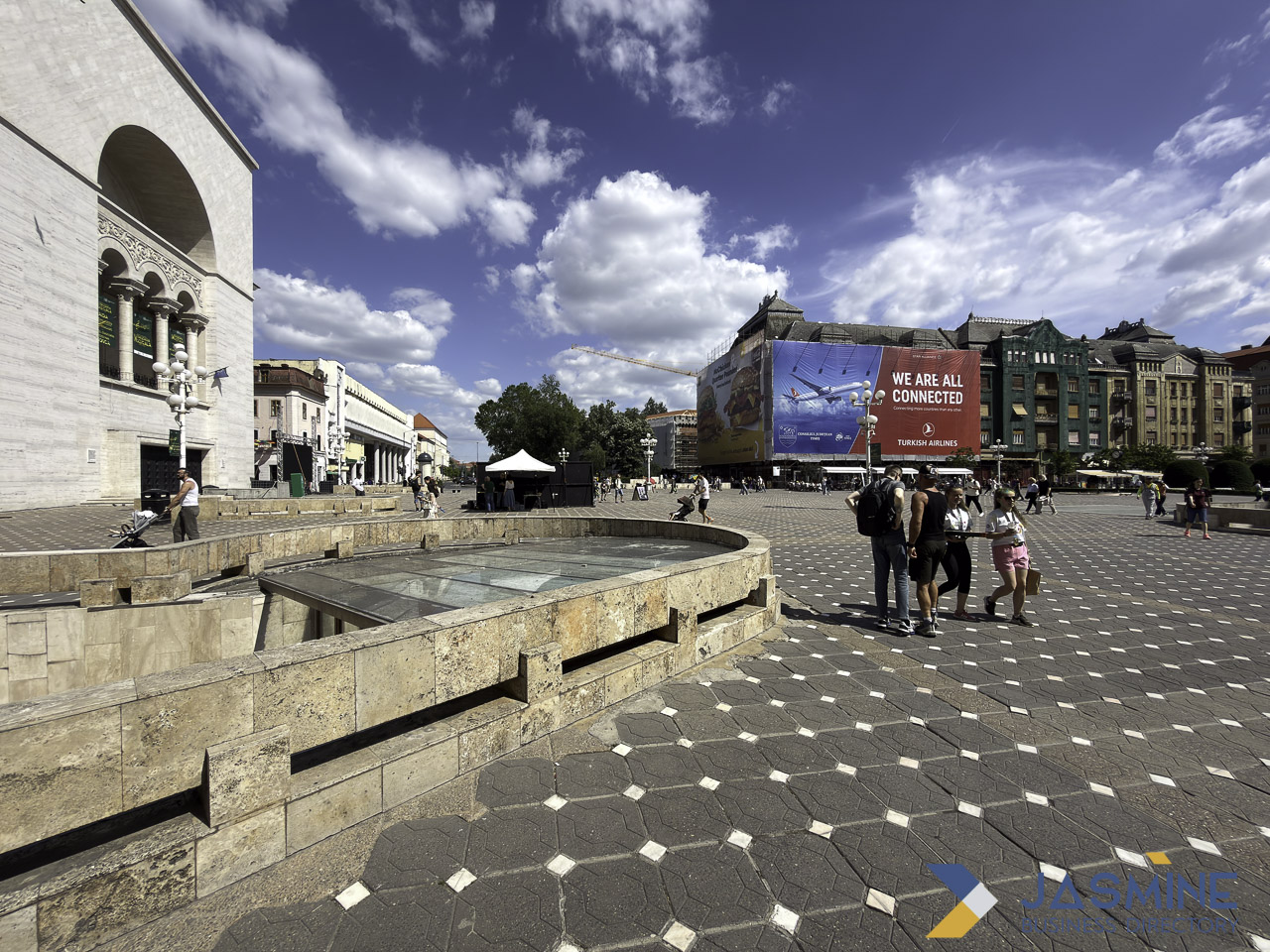 Public plaza in Timișoara with fountain and church, featuring a large billboard advertisement on building facade, demonstrating outdoor advertising in urban environments.