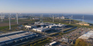 Sustainability in Advertising: Reducing the Carbon Footprint of Your Campaigns Aerial view of a coastal industrial park with multiple wind turbines and warehouse facilities, illustrating renewable energy integration in commercial infrastructure for carbon footprint reduction.