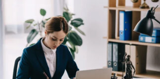 Professional woman in blazer works at desk with laptop and legal symbols, representing the research process for selecting law business directories.