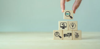 Hand placing a wooden block with SEO icon at the top of a pyramid of business marketing cubes, representing premium placement strategy in business directories.