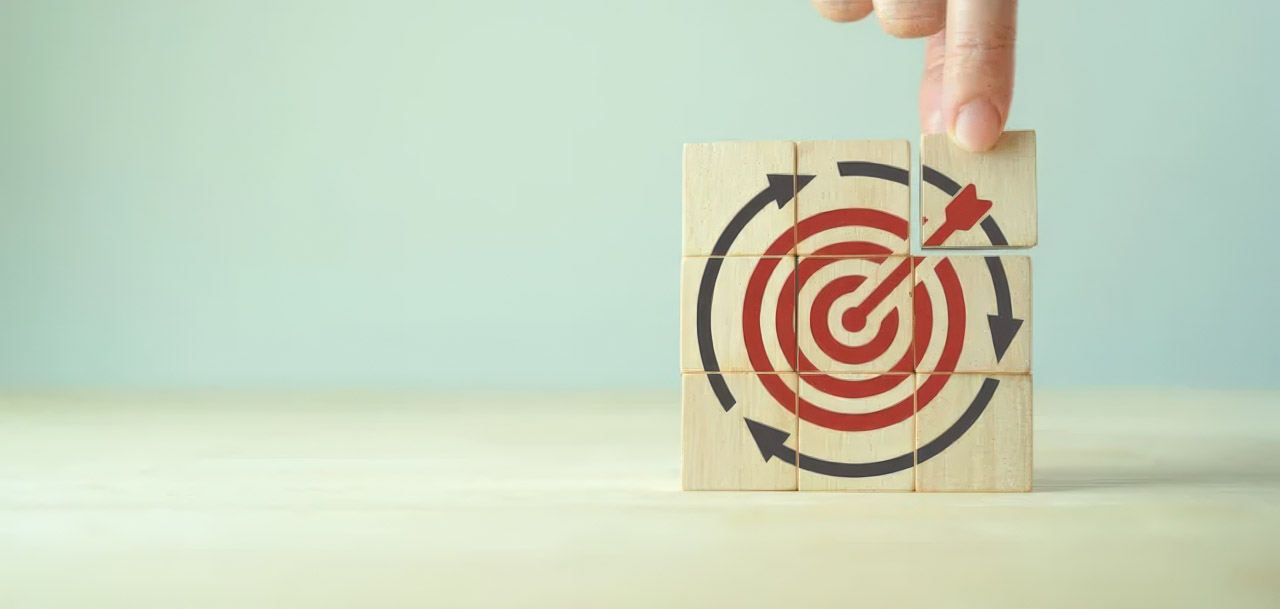Hand touching wooden blocks printed with a target and dart bullseye design, representing focused goal-setting for efficient marketing strategy development.