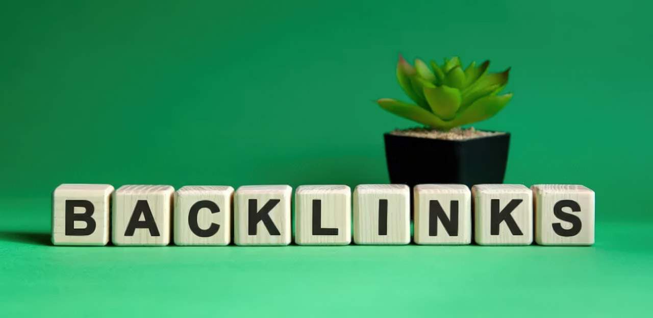 Wooden letter blocks spelling BACKLINKS on a green surface with a succulent plant, representing link building strategies for website authority and SEO.
