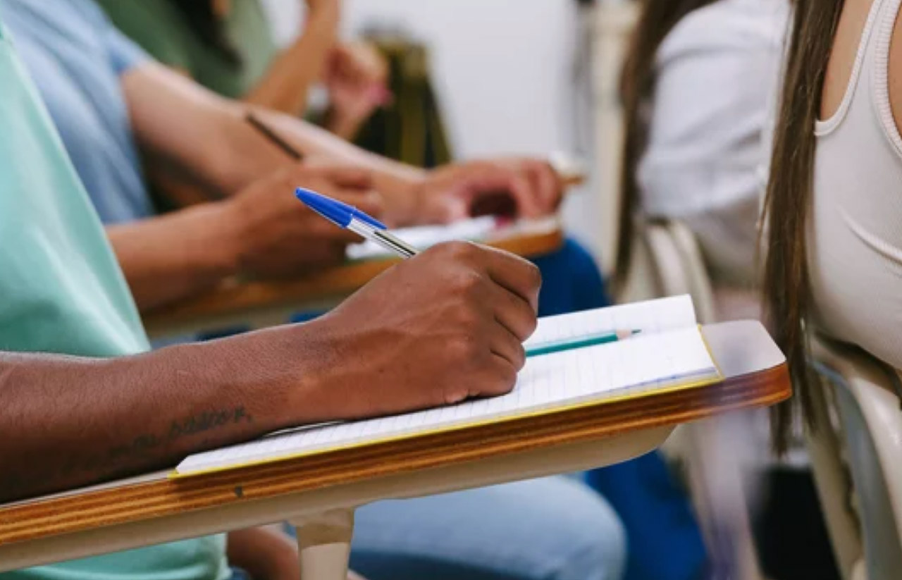 Close-up of hands writing on clipboard during group workshop session, representing collaborative content creation strategies for dual human and AI audiences.